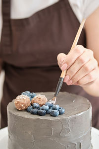 Woman pastry chef decorates grey cake with blueberries and glitter, close-up. cake making process