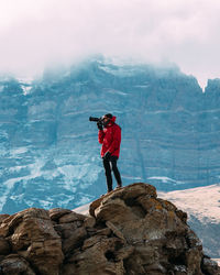 Man photographing with digital camera while standing on rock against mountain