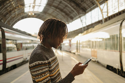 Young man using smart phone while standing at railroad station platform