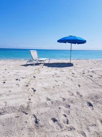 Deck chairs on beach against clear blue sky