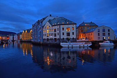 Canal by illuminated buildings against sky at dusk