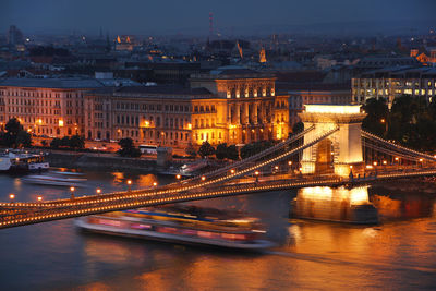 Illuminated bridge over river in city at night