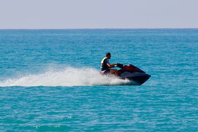 Young man riding motorboat on sea against clear blue sky during sunny day