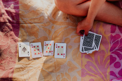 Top view of crop anonymous female having combination of ace of spades and 4 5 6 of hearts cards while playing game on blanket on beach