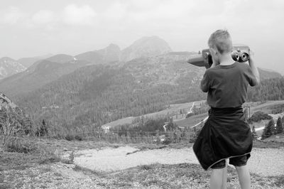 Rear view of boy looking at mountains through coin-operated binocular