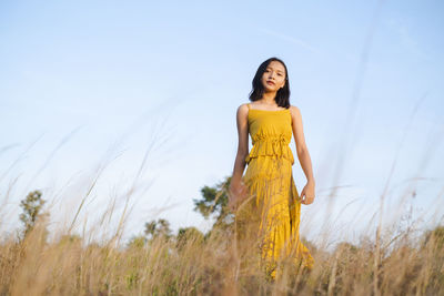 Young woman standing on field against sky