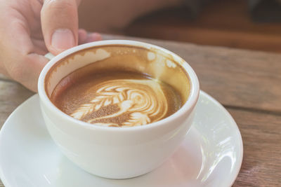 Close-up of hand holding coffee cup on table