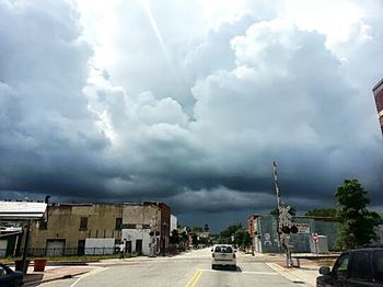 Road passing through city against cloudy sky