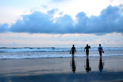 Silhouette friends walking on beach against sky