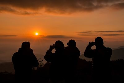 Silhouette people photographing sunset
