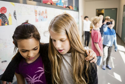 Girls walking with arms around against friends in corridor at school