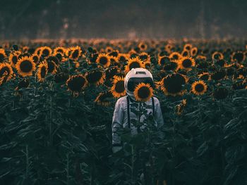 Astronaut standing amidst sunflowers blooming on field