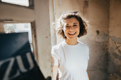 Portrait of smiling young woman standing against white wall