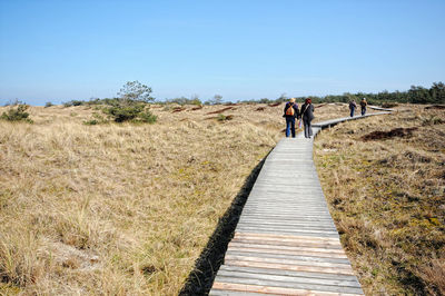 Rear view of women walking on boardwalk at field against sky