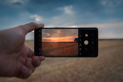 Cropped image of hand holding camera phone against sky