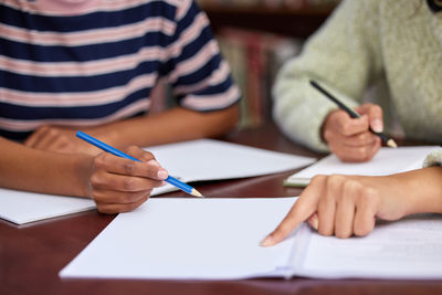 Midsection of woman writing in book at table