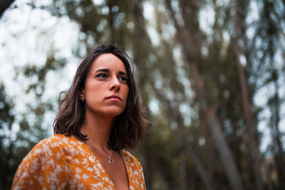 Young woman looking away while standing against tree