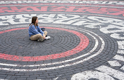 Young woman in blue sweatshirt alone sitting on street cobbled square, introvert