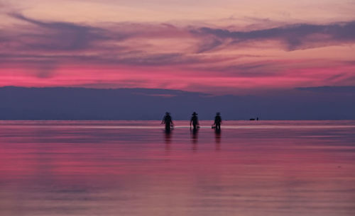 Silhouette people on sea against sky during sunset