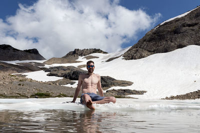 Man sitting in lake against mountains during winter