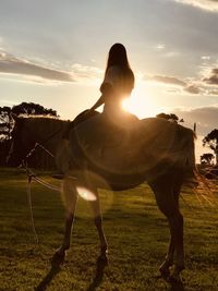 Man riding horse on field against sunset sky