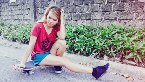 Young woman sitting on skateboard by plants