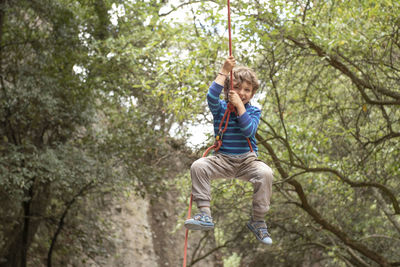 Four year old smily toddler plays hanging from a climbing rope