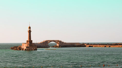 Lighthouse by sea against clear sky