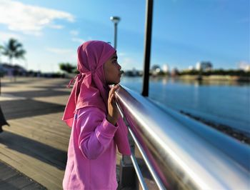 Side view of woman standing by pink umbrella against sky