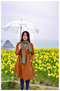 Portrait of woman holding umbrella while standing against yellow flowers on land
