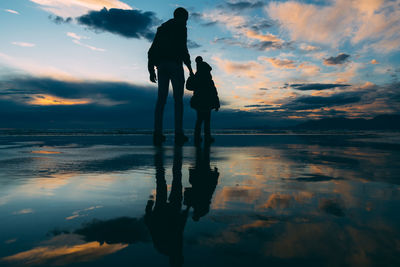 Silhouette woman standing on sea against sky during sunset
