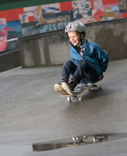 Full length of happy woman sitting on skateboard