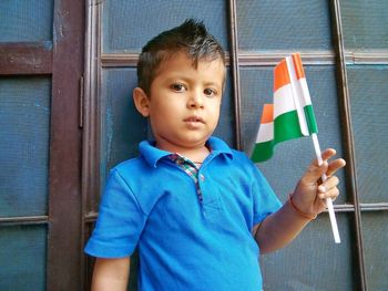 Portrait of cute boy with indian flag standing against wall