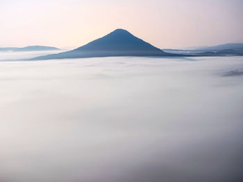 Sharp cone hill growing up from misty flat land. magnificent foggy daybreak