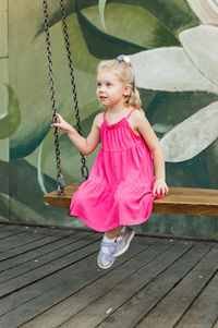 Portrait of cute girl sitting on wooden wall