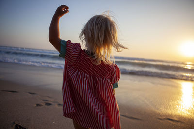 Rear view of child running on beach against sky