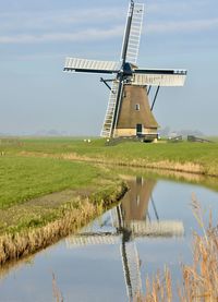 Traditional windmill by lake against sky