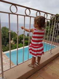 Rear view of boy standing on railing against sky