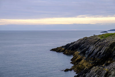 Two people standing on a cliff looking out to the ocean