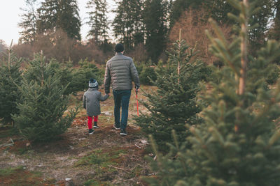 Rear view of father with son walking on field in forest