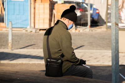 Side view of man wearing hat sitting in city