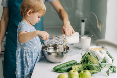 Toddler daughter beats eggs with a whisk helping mom prepare an omelette.