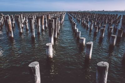 Wooden posts in sea against sky