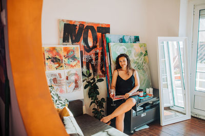 Artist sitting in home studio surrounded by canvas and paintings