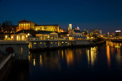 Illuminated cityscape by river against sky at night