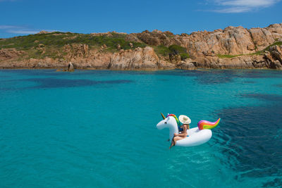 Woman sitting on inflatable unicorn in aegean sea against sky