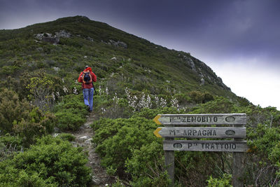 Rear view of hiker walking on mountain against cloudy sky