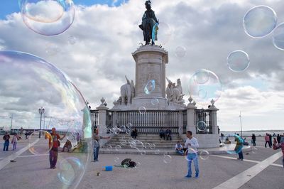 People playing with bubbles against sky in background