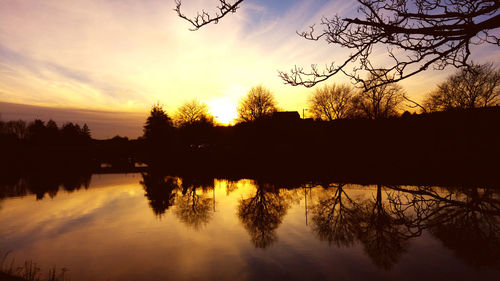 Silhouette trees by lake against sky during sunset