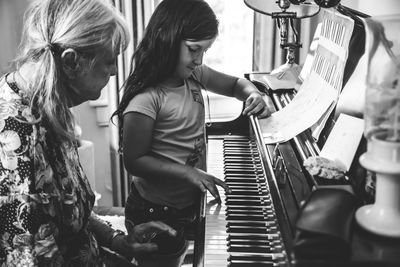 Grandmother teaching piano to granddaughter at home